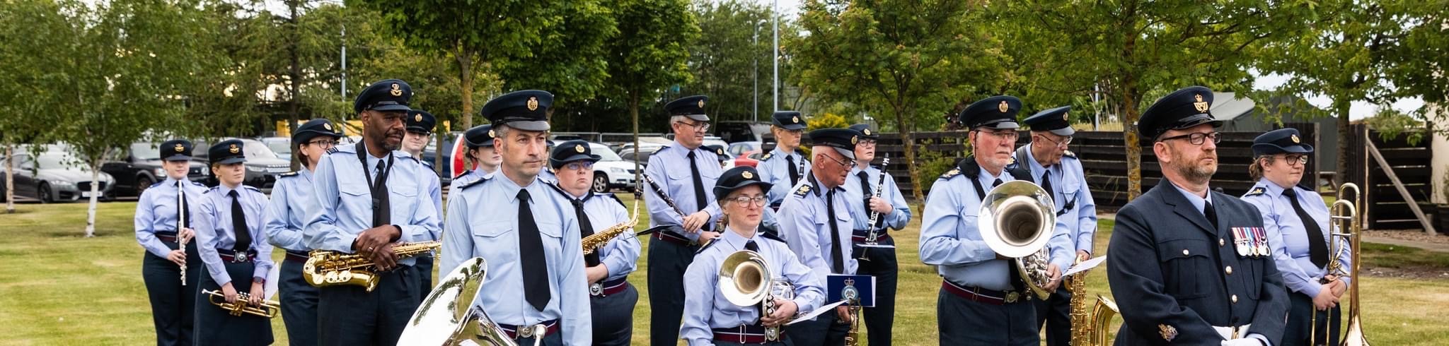 Image shows RAF brass band parading past car park.